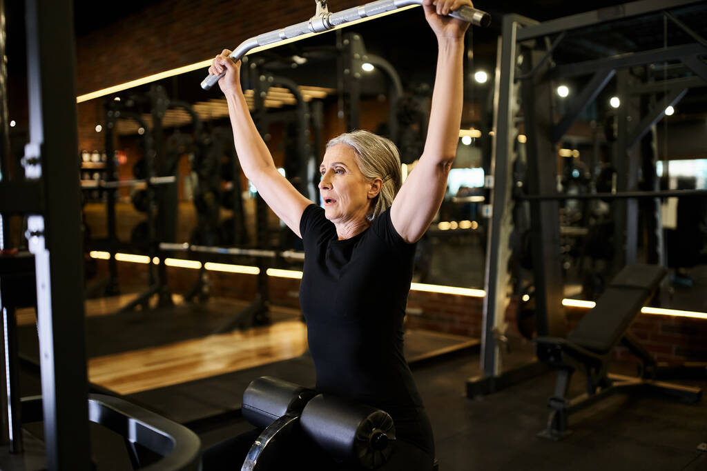 atractiva mujer mayor deportivo en traje acogedor ejercicio activo con lats máquina de extracción en el gimnasio - Foto, Imagen