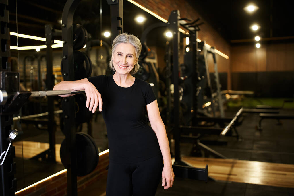 fröhliche ältere attraktive Frau in Sportbekleidung posiert im Fitnessstudio und lächelt glücklich in die Kamera - Foto, Bild