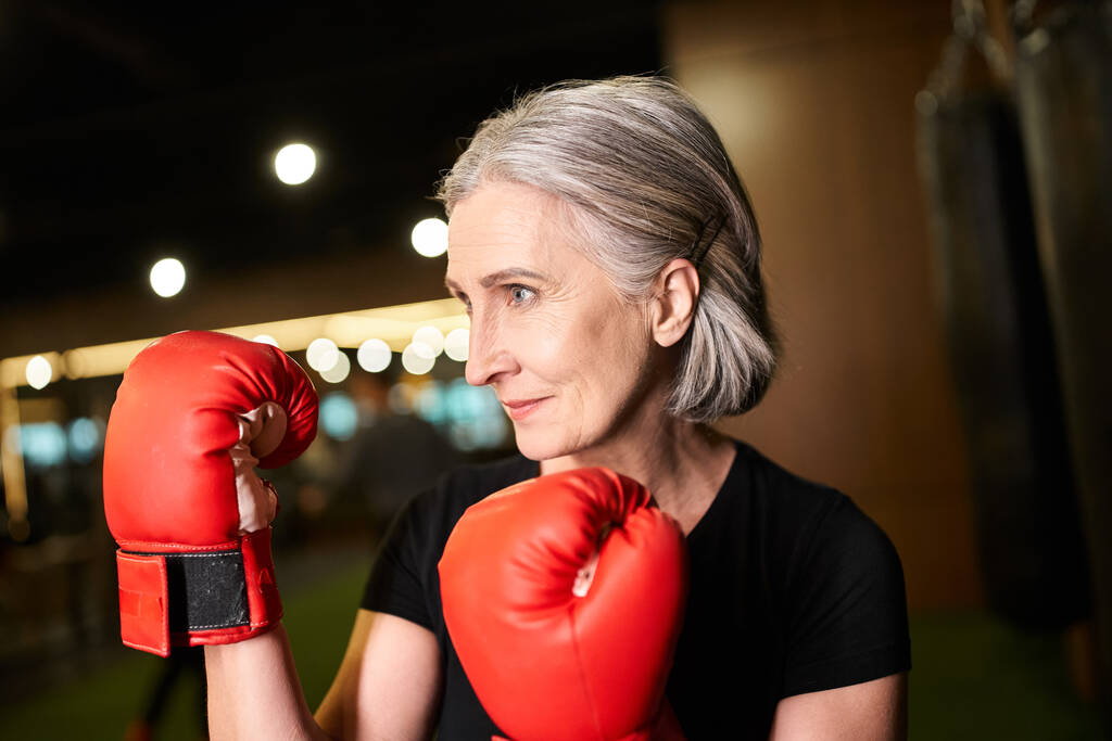 sportlich gut aussehende Seniorin mit grauen Haaren posiert mit Boxhandschuhen beim Training im Fitnessstudio - Foto, Bild