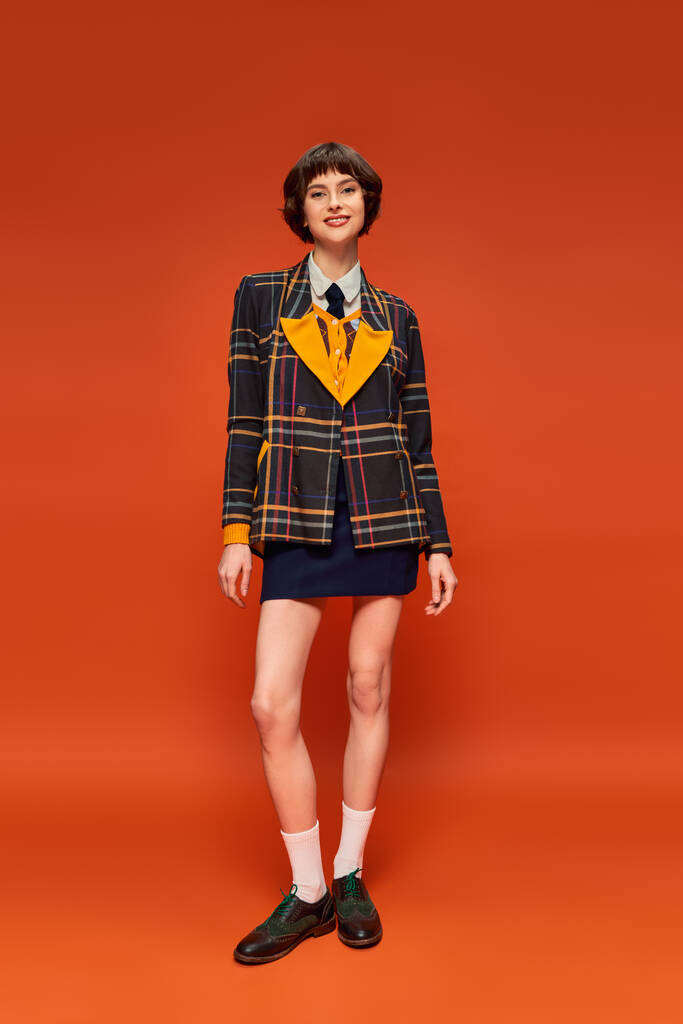 Portakal rengi arka planda çorapları olan kareli ceketli ve ayakkabılı üniversiteli bir kız. - Fotoğraf, Görsel