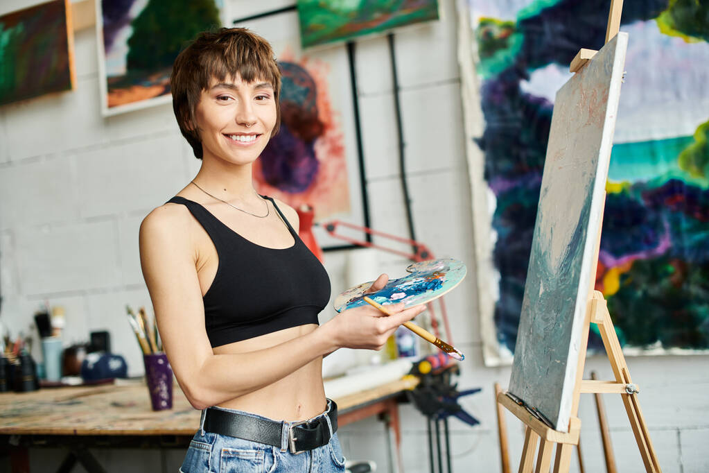 Una mujer sostiene un pincel delante de una pintura. - Foto, Imagen