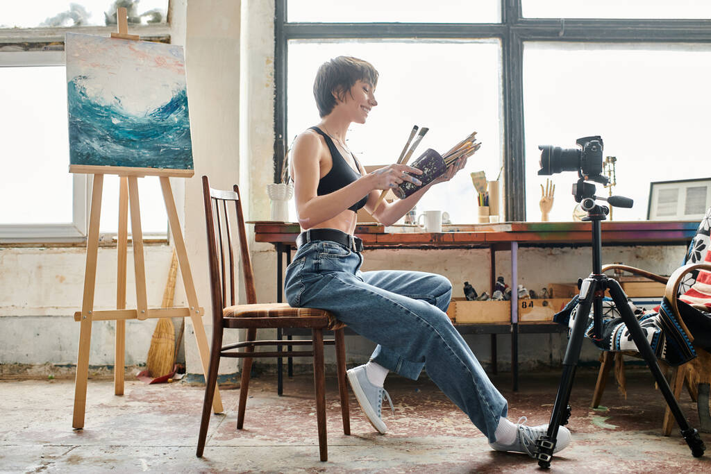 Csinos nő ül a székben, megmutatja, hogyan kell festeni a kamera. - Fotó, kép