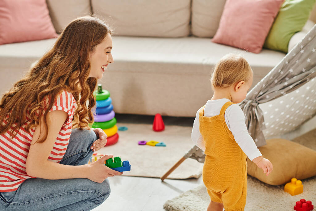 Een jonge moeder gaat vrolijk met haar peuter dochter in vrolijk spelen in een gezellige woonkamer omgeving. - Foto, afbeelding