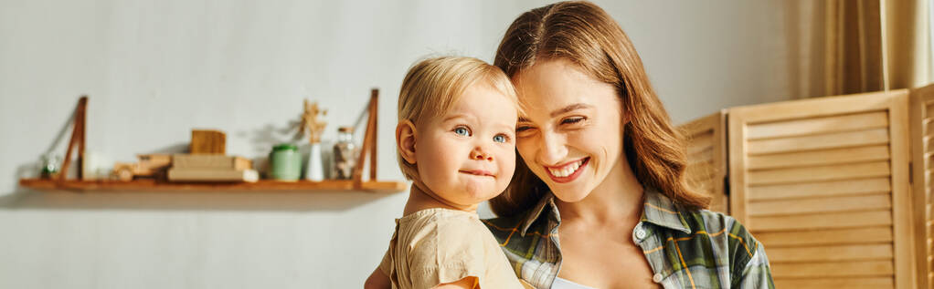 Mladá matka něžně drží svou batolata dceru v náručí, sdílí vzácný okamžik lásky a spojení doma. - Fotografie, Obrázek