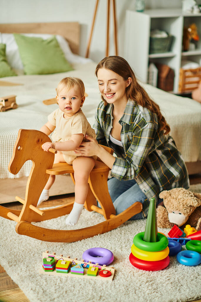A young mother joyfully plays with her toddler daughter on a rocking horse, sharing laughter and creating cherished memories. - Photo, Image