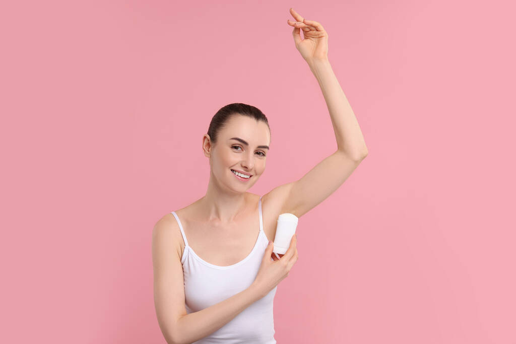 Hermosa mujer aplicando desodorante sobre fondo rosa - Foto, imagen