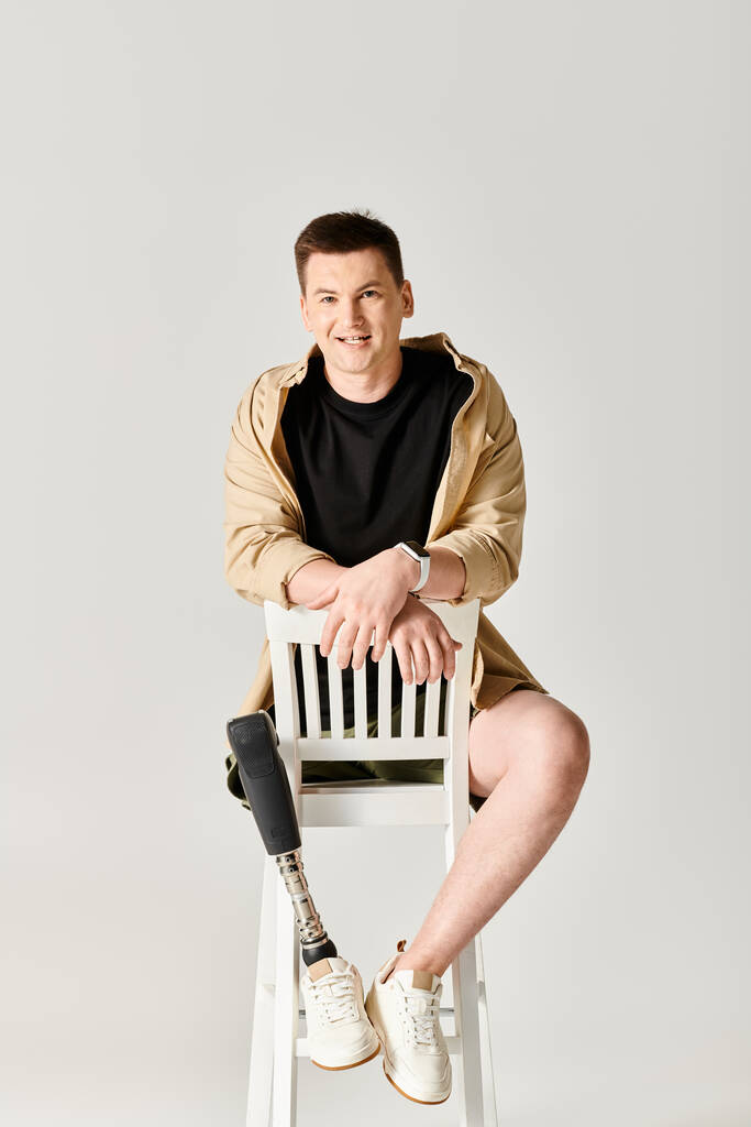 Un hombre guapo con una pierna protésica se sienta con confianza sobre una silla blanca. - Foto, Imagen