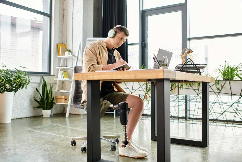 Przystojny biznesmen z protezą nogi siedzi przy biurku, skupiony na pracy na laptopie.. - Zdjęcie, obraz