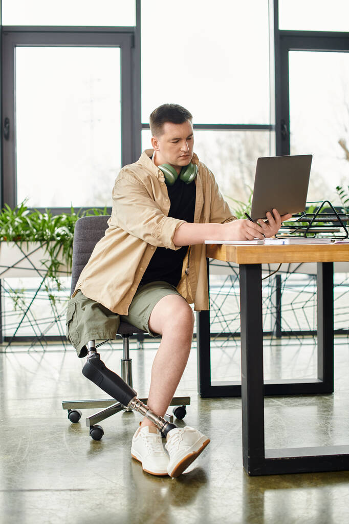 A businessman with a prosthetic leg concentrates while using a laptop at a table. - Photo, Image