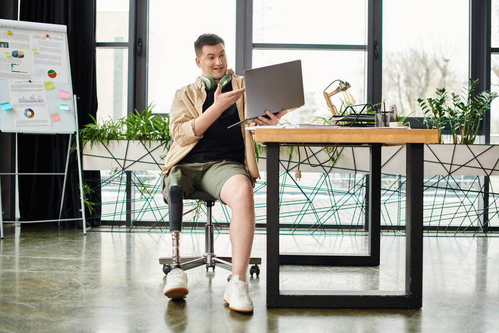 Een knappe zakenman met een kunstbeen aan een bureau, gericht op het gebruik van een laptop. - Foto, afbeelding