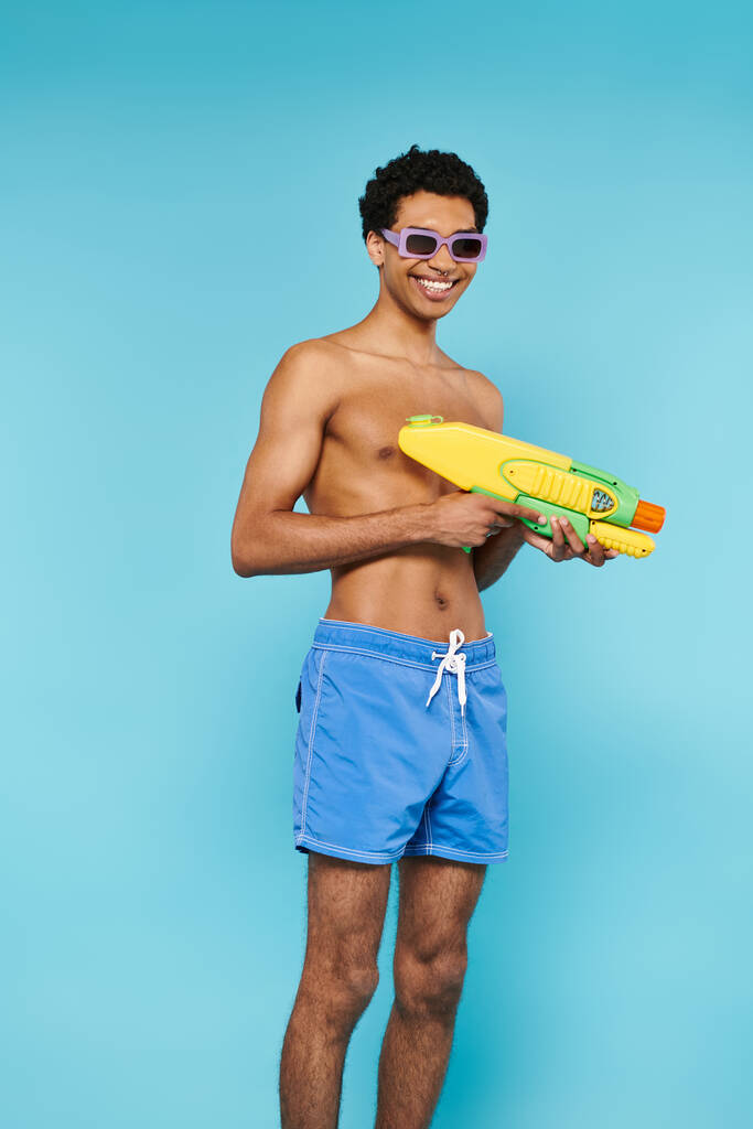 iloinen nuori afrikkalainen amerikkalainen mies uimahousut tyylikäs aurinkolasit poseeraa vesipyssy - Valokuva, kuva
