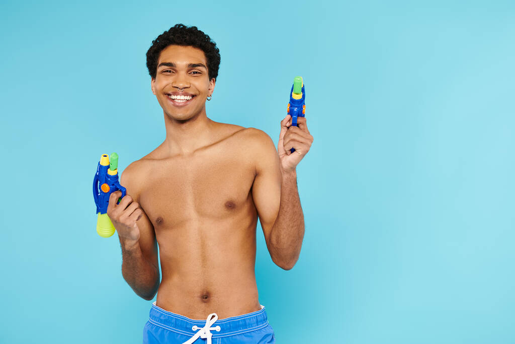 alegre bonito afro-americano homem posando com duas armas de água e sorrindo para a câmera feliz - Foto, Imagem