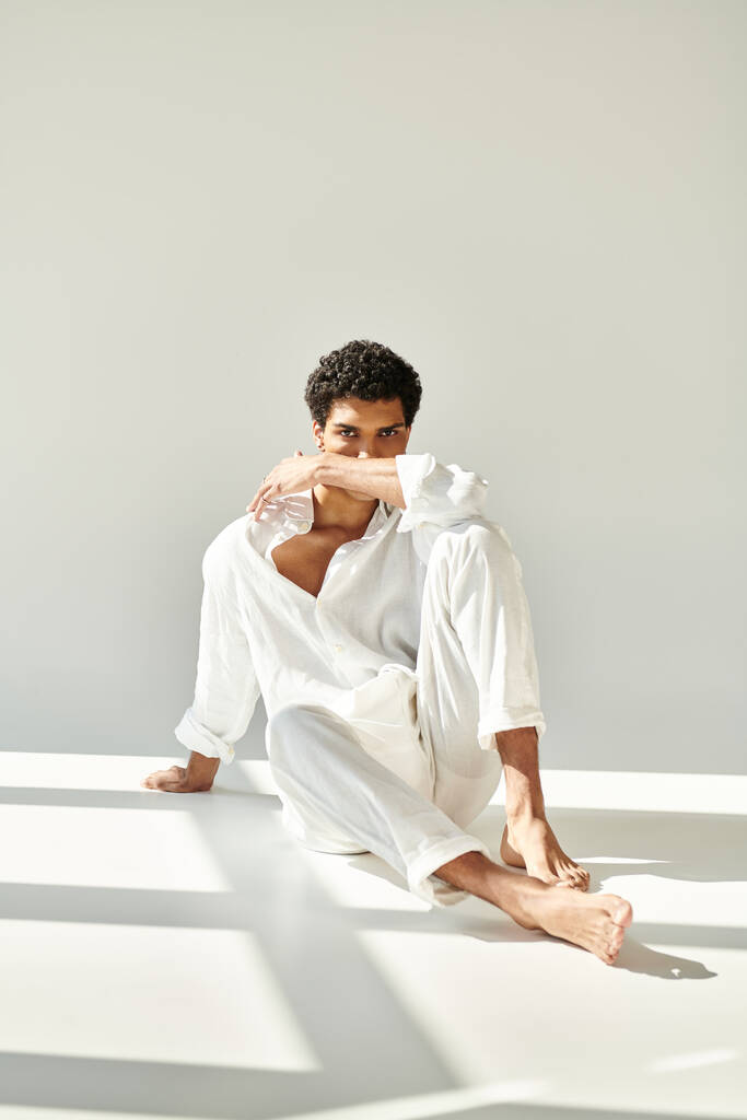 přitažlivý sofistikovaný africký Američan v plátně oblečení sedí na podlaze a dívá se do kamery - Fotografie, Obrázek