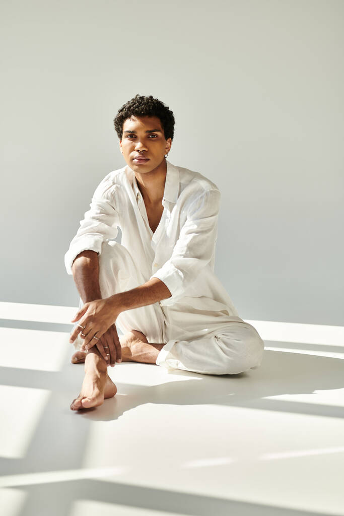 smaakvolle jonge Afrikaanse Amerikaanse man in linnen kleding kijken naar camera op de vloer op beige achtergrond - Foto, afbeelding