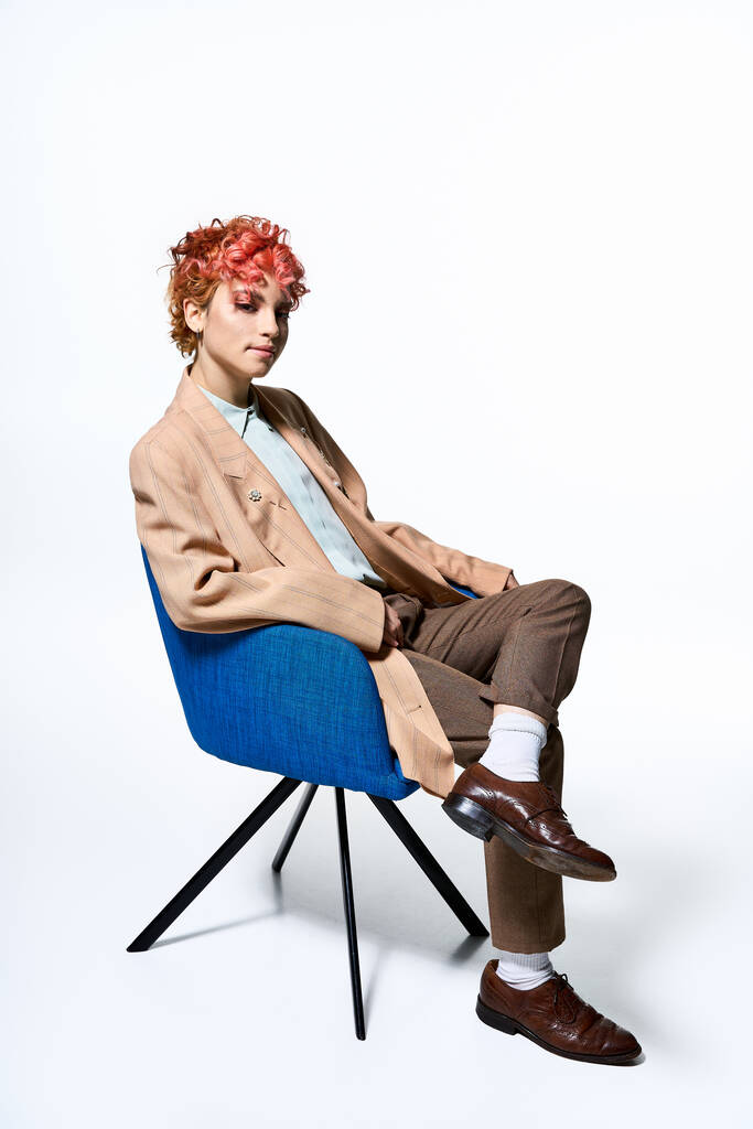 Mujer extraordinaria con el pelo rojo ardiente se relaja en una silla azul elegante. - Foto, Imagen