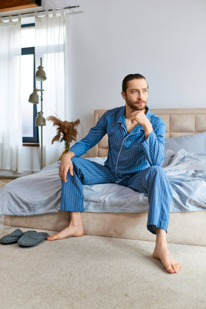 Un bel homme en pyjama s'assoit calmement sur un lit. - Photo, image