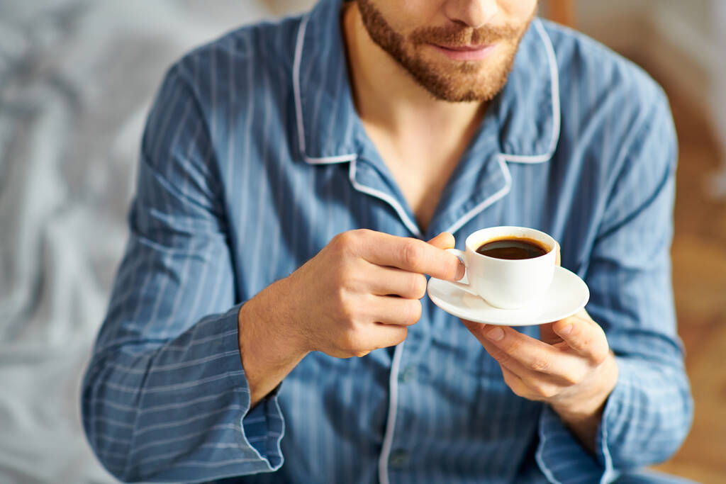 Un hombre guapo en pijama disfrutando pacíficamente de una taza de café. - Foto, imagen