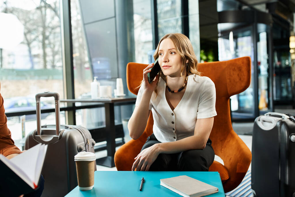 Una mujer con colegas, sentada en una silla, conversando en su celular durante un viaje corporativo. - Foto, imagen