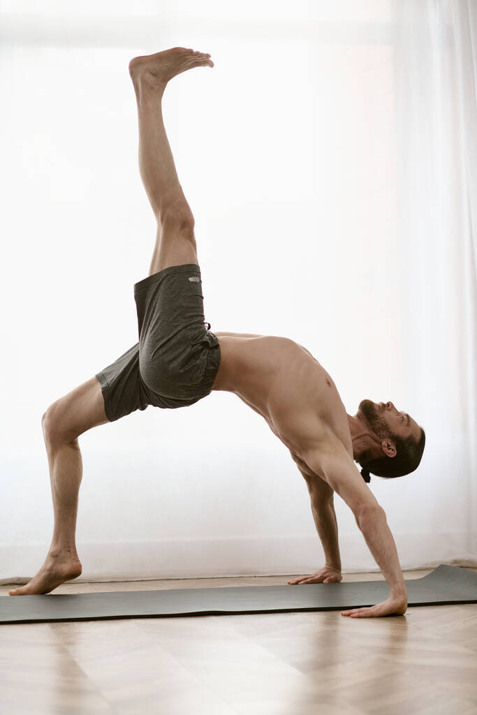 Un hombre guapo practica un soporte de mano en una esterilla de yoga en su casa. - Foto, imagen