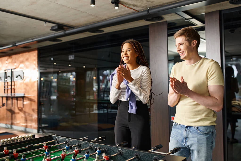 Un hombre y una mujer de un equipo de startups diseñan estrategias alrededor de una mesa de futbolín en un moderno espacio de coworking. - Foto, imagen