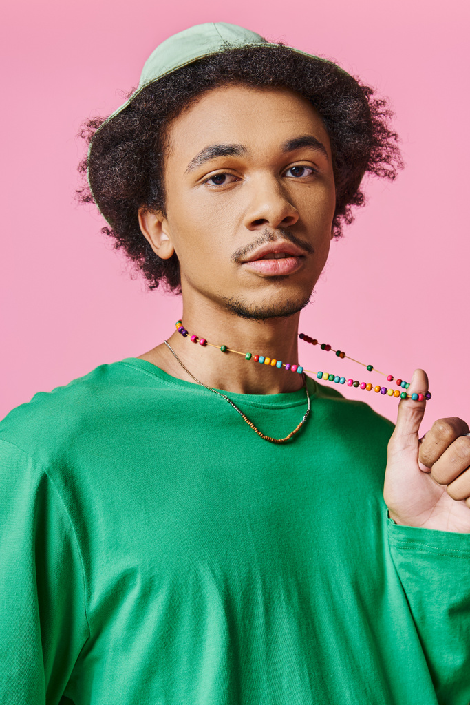 Kıvırcık saçlı, yeşil tişörtlü ve pembe arka planda boncuklu kolyesi olan genç bir Afrikalı Amerikalı.. - Fotoğraf, Görsel