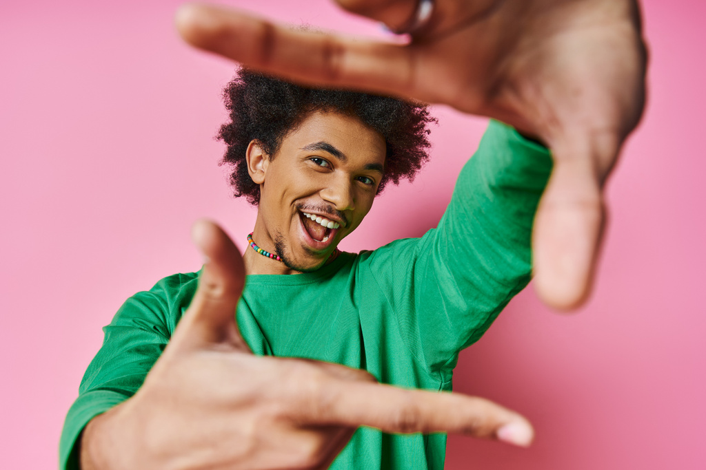 Um jovem e alegre afro-americano vestido casualmente em um fundo rosa faz um gesto com as mãos, exibindo várias emoções.. - Foto, Imagem