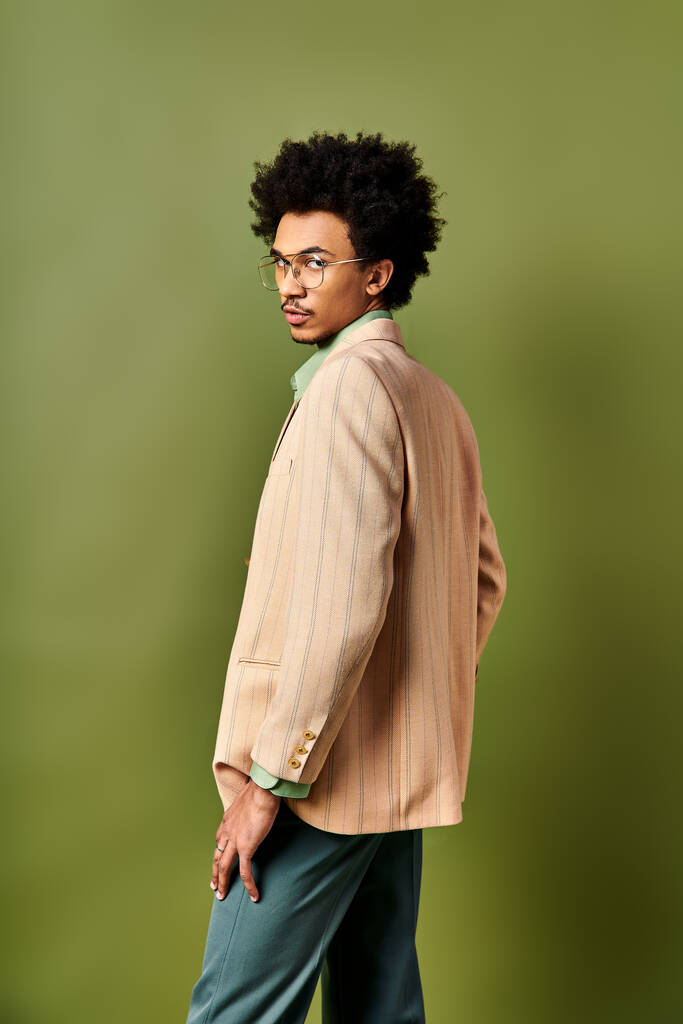 Elegante hombre afroamericano con pelo rizado y gafas, exuda confianza en traje de moda sobre fondo verde. - Foto, Imagen