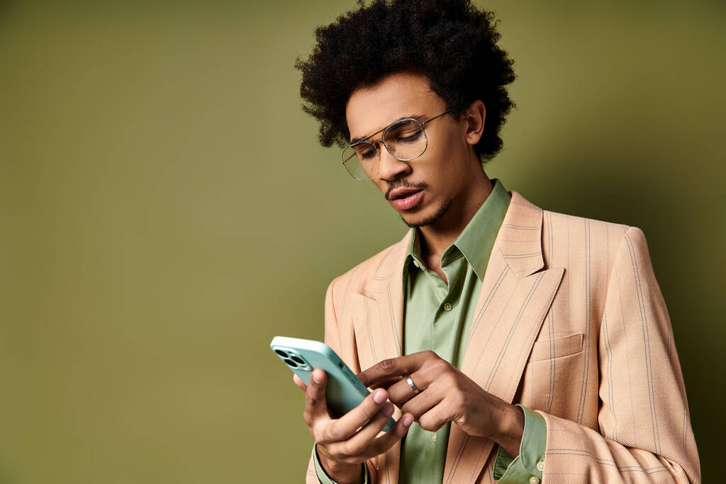 Un giovane uomo afroamericano elegante in giacca e cravatta e occhiali da sole, utilizzando un telefono cellulare su sfondo verde. - Foto, immagini