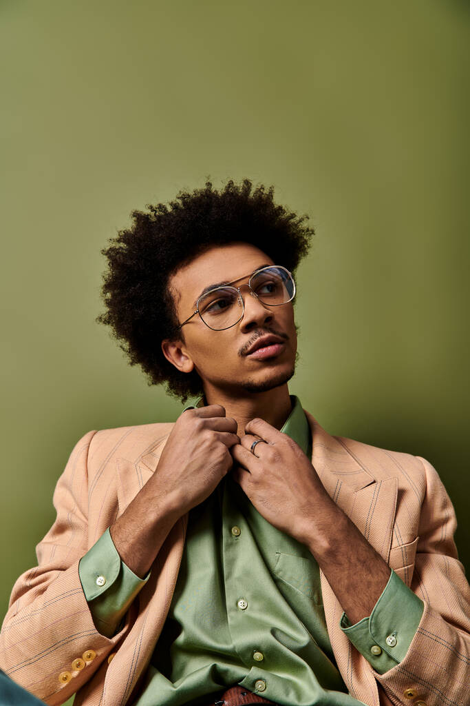 Egy elegáns, fiatal afro-amerikai férfi öltönyben és szemüvegben leül, magabiztosságot és kifinomultságot árasztva.. - Fotó, kép