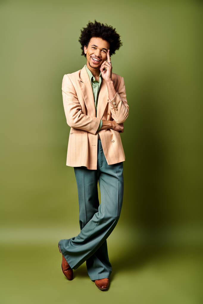Módní mladý Afroameričan s kudrnatými vlasy v opálené bundě, zelené kalhoty na zeleném pozadí. - Fotografie, Obrázek