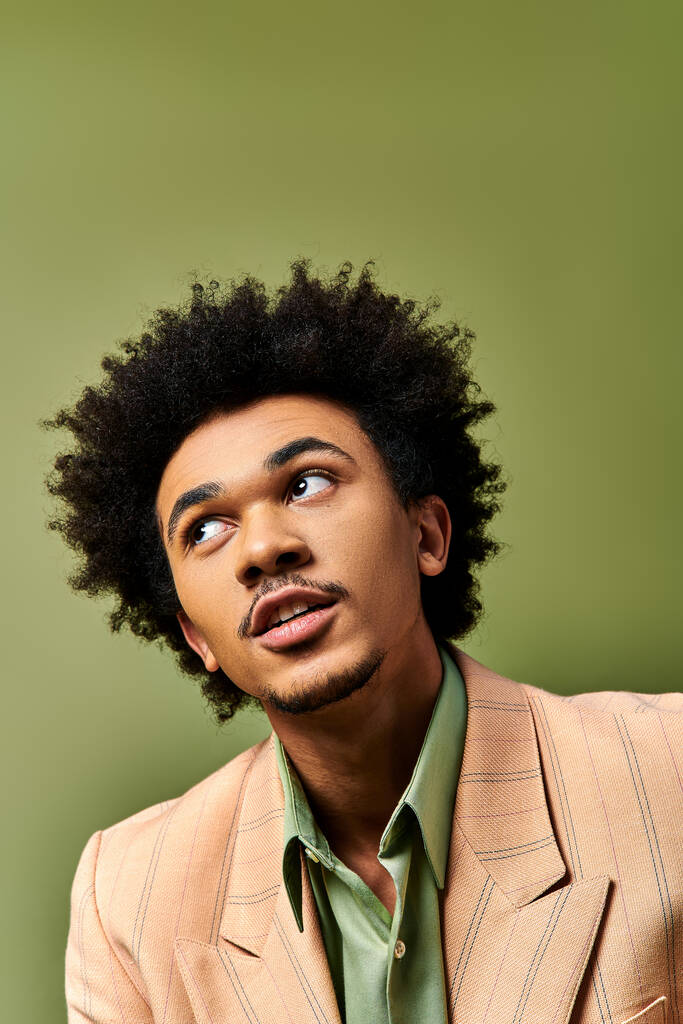 Um jovem afro-americano elegante com cabelo encaracolado parece surpreso contra um fundo verde. - Foto, Imagem