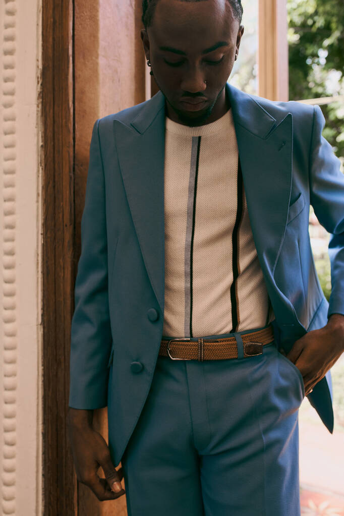 Beau Afro-Américain en costume bleu debout élégamment à côté d'une porte. - Photo, image