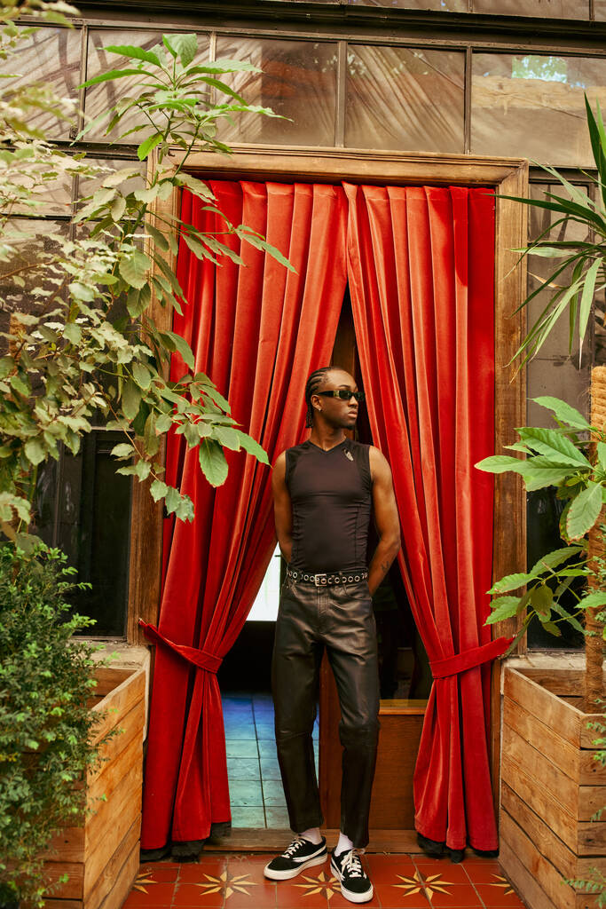 Un apuesto afroamericano posa frente a una vibrante cortina roja. - Foto, Imagen
