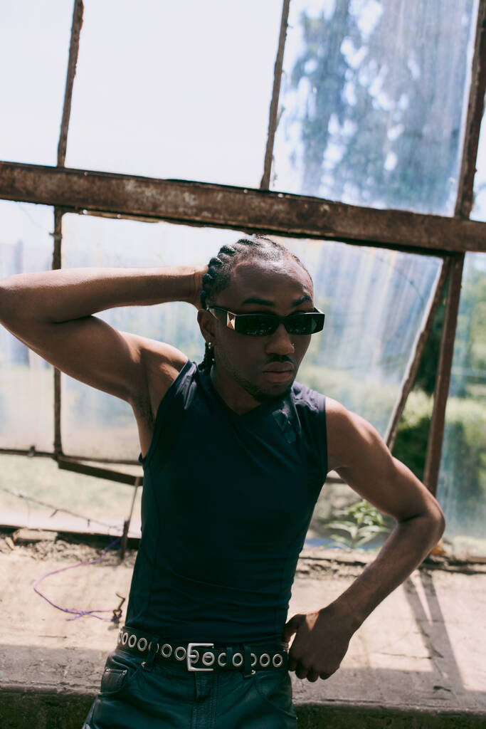 Dapper Afroameričan v černé košili a slunečních brýlích pózující sebevědomě v zářivé zelené zahradě. - Fotografie, Obrázek