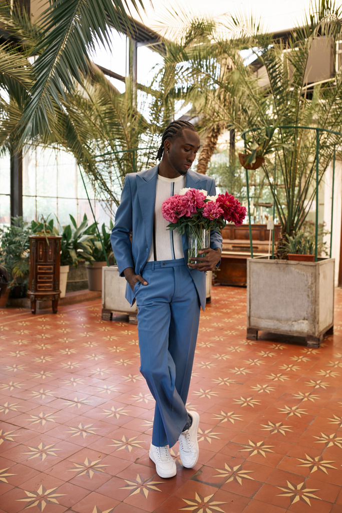 Schöner afroamerikanischer Mann im blauen Anzug mit Blumen in einem lebhaften grünen Garten. - Foto, Bild