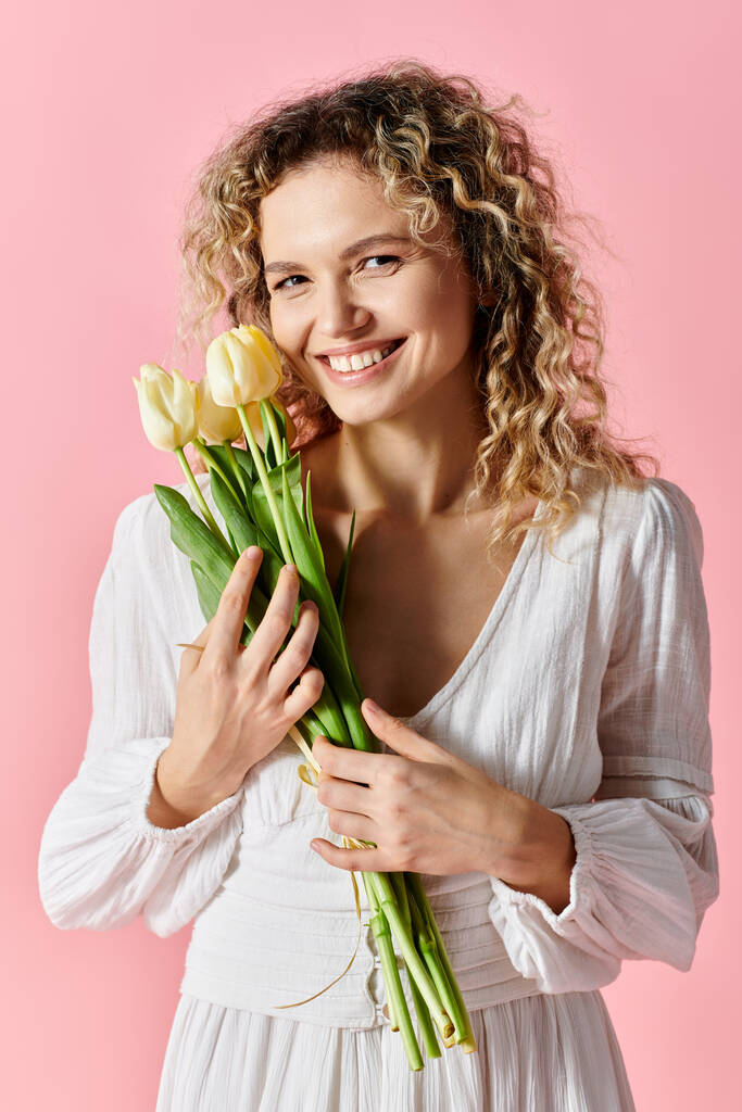 Женщина на розовом фоне держит букет ярких тюльпанов. - Фото, изображение