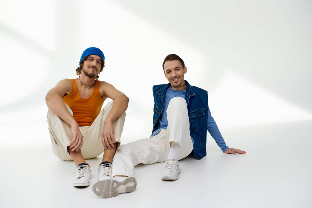 appealing joyful lgbtq friends in stylish outfits posing on gray backdrop and looking at camera - Photo, Image