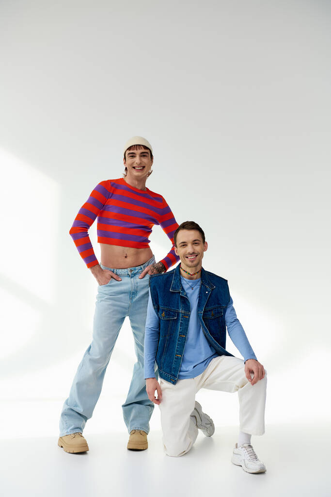 two joyful good looking lgbt friends in vibrant attires looking at camera posing on gray backdrop - Photo, Image