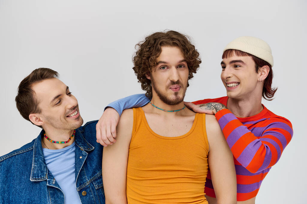 pozytywne młody gej mężczyźni w żywe odzież pozowanie razem na szary tło i patrząc w kamery - Zdjęcie, obraz