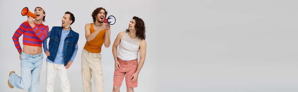 čtyři veselí gayové ve stylových šatech, kteří používají megafony a aktivně pózují na šedém pozadí, banner - Fotografie, Obrázek