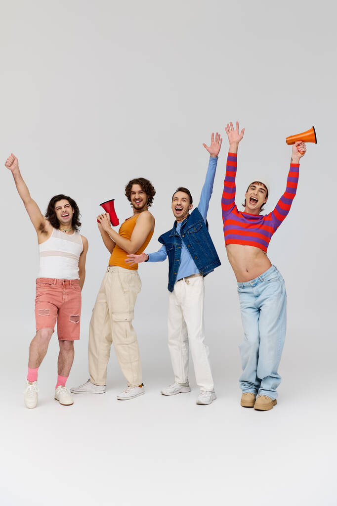 cuatro alegre de moda gay los hombres en elegante trajes usando megáfonos y mirando a la cámara felizmente - Foto, Imagen
