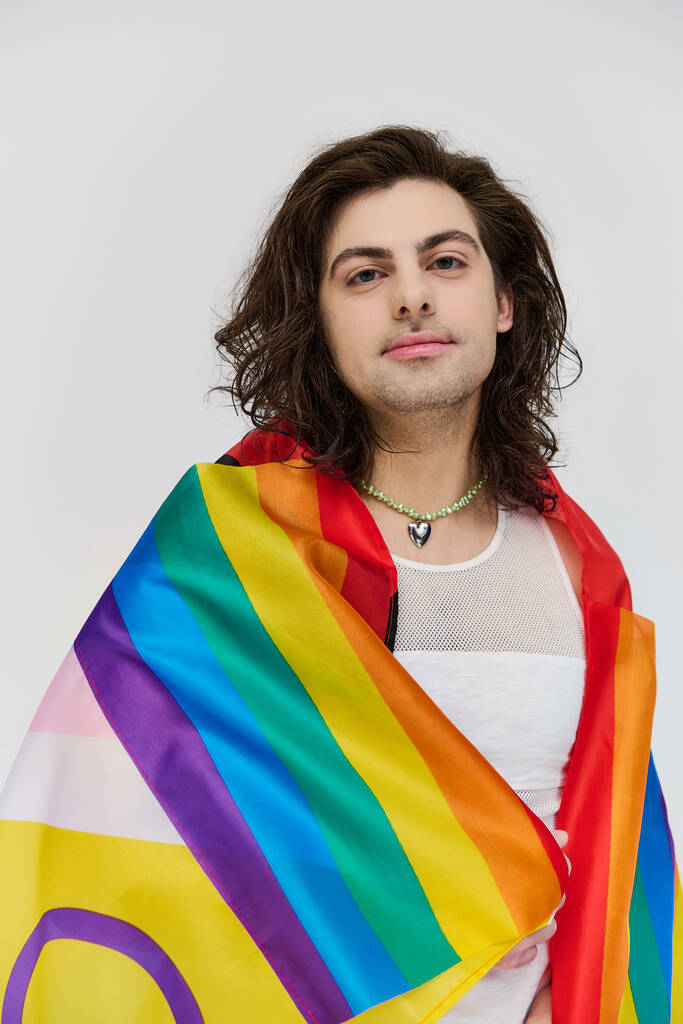good looking joyous gay man with long dark hair posing with rainbow flag and looking at camera - Photo, Image
