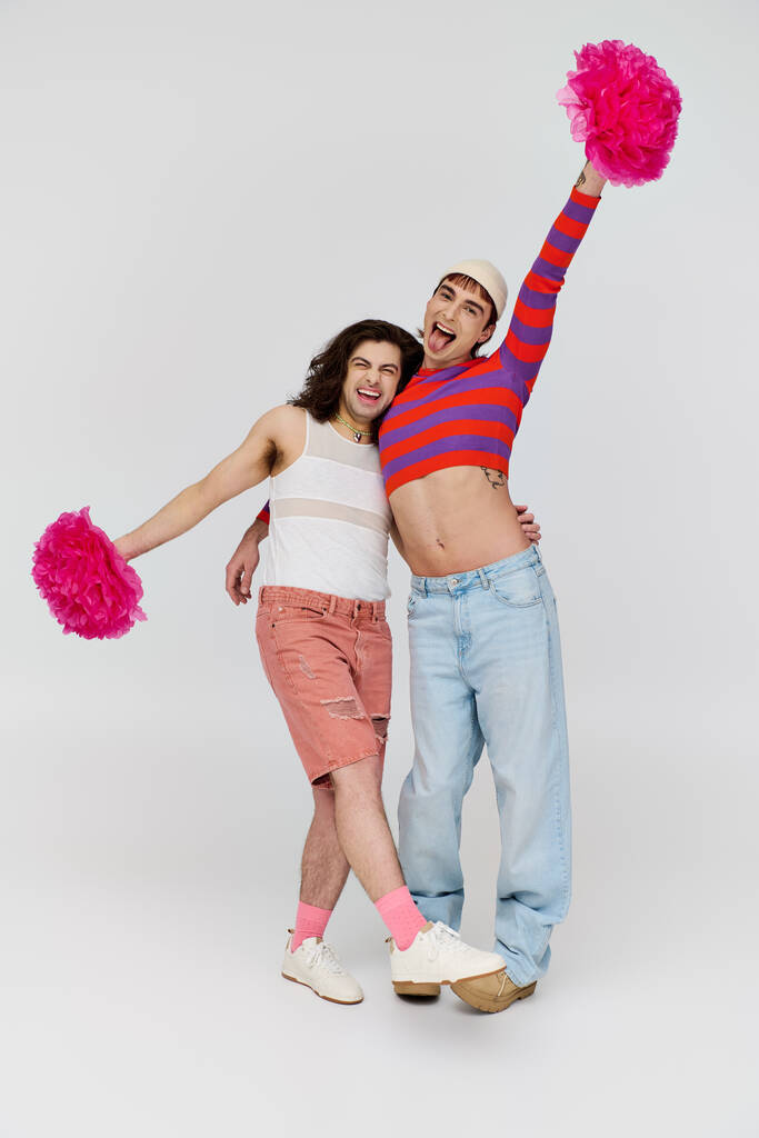 веселые молодые геи в повседневных ярких одеждах счастливо позируют с помпонами и смотрят в камеру - Фото, изображение