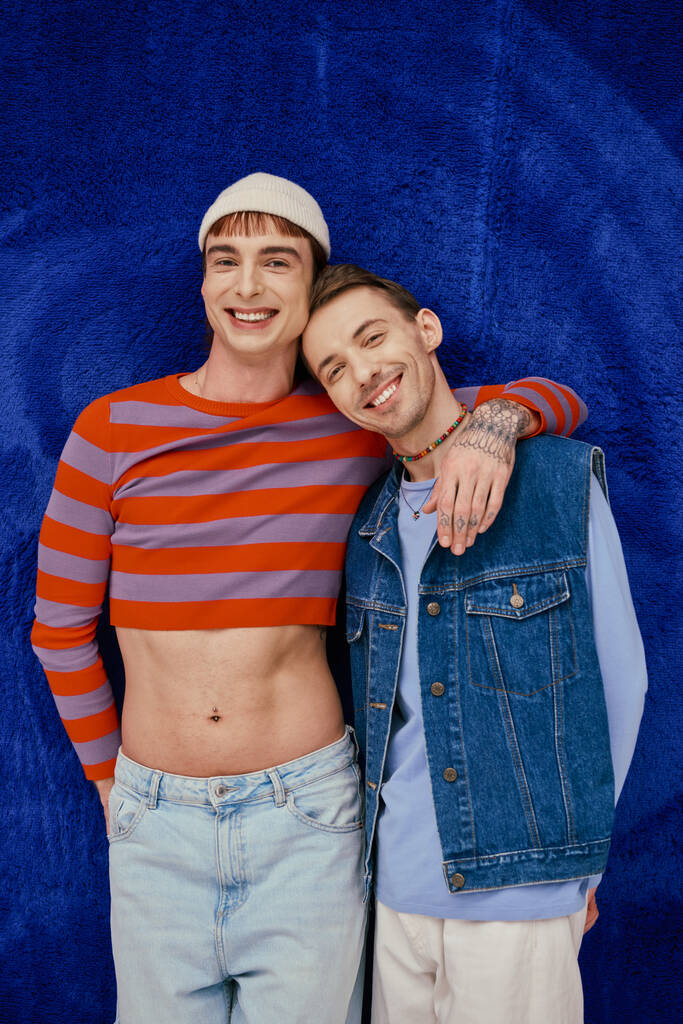 twee positieve goed uitziende gay mannen in levendige kleding poseren op donkerblauwe achtergrond, trots maand - Foto, afbeelding