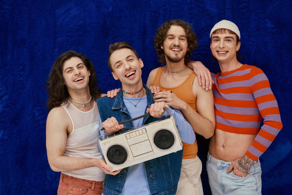 τέσσερις voguish χαρούμενους γκέι φίλους ποζάρουν με μαγνητόφωνο σε σκούρο μπλε φόντο, μήνα υπερηφάνειας - Φωτογραφία, εικόνα