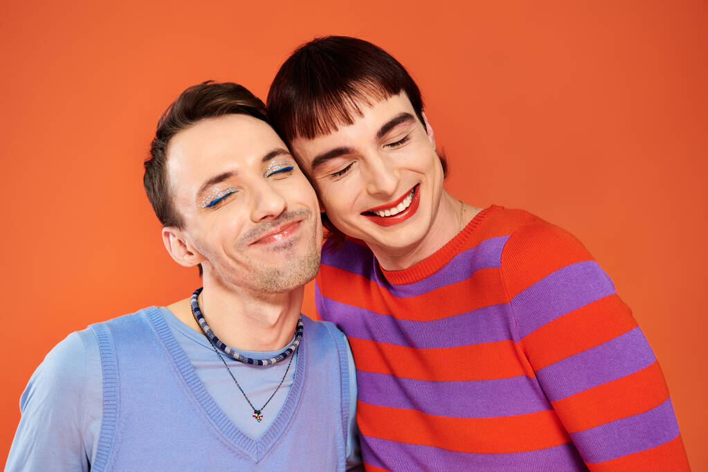 positive attractive gay friends with vivid makeup posing together on orange backdrop, pride month - Photo, Image