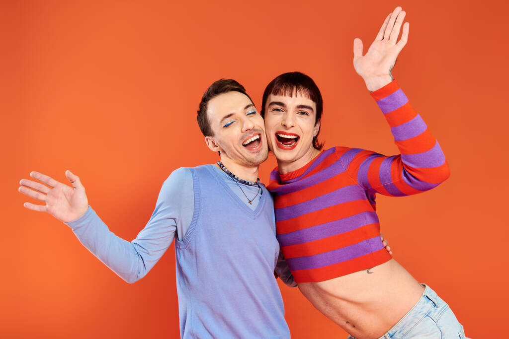 cheerful attractive gay friends with vivid makeup posing together on orange backdrop, pride month - Photo, Image