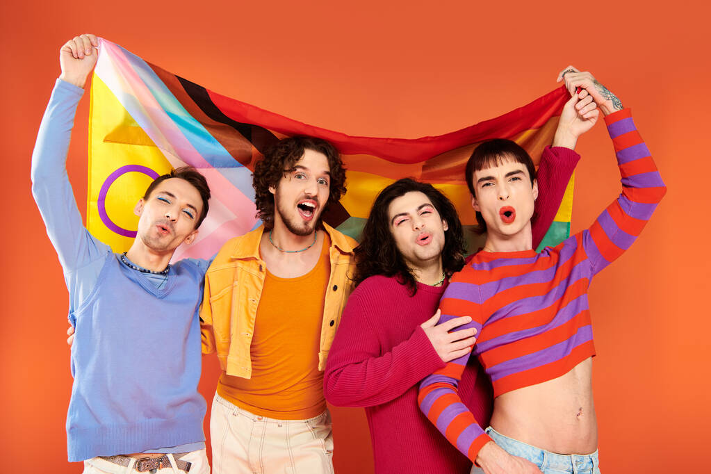 quattro gioiosi uomini gay alla moda in abiti vibranti con bandiera arcobaleno davanti alla telecamera, orgoglio - Foto, immagini