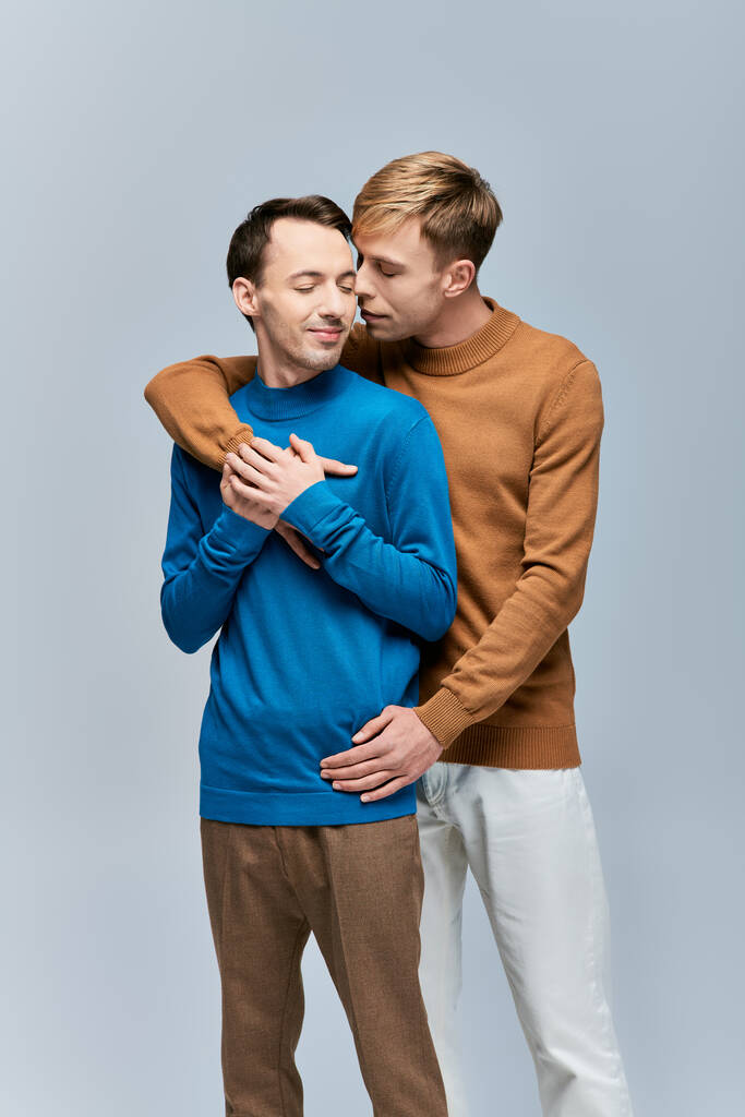 Αγαπώντας γκέι ζευγάρι σε casual ενδυμασία στέκεται δίπλα-δίπλα σε ένα γκρι φόντο. - Φωτογραφία, εικόνα