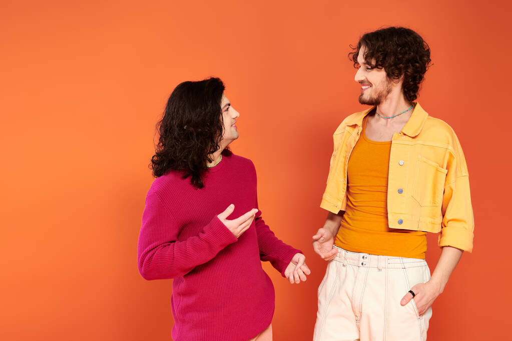χαρούμενους νεαρούς γκέι φίλους με κομψά, ζωντανά ρούχα που ποζάρουν μαζί σε πορτοκαλί φόντο, υπερηφάνεια - Φωτογραφία, εικόνα